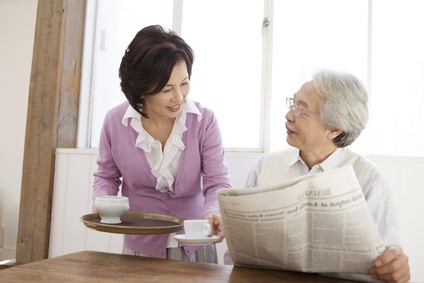 新聞を読む初老の男性とお茶を入れる妻